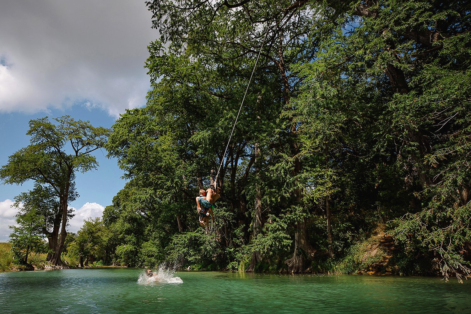 4 boys swinging over the river in Dripping Springs, Texas